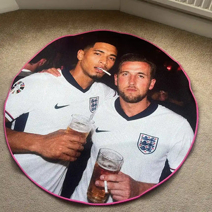 A circular floor mat featuring a printed photo of England football players Jude Bellingham and Harry Kane in white jerseys, placed on a beige carpeted floor in front of a white radiator.