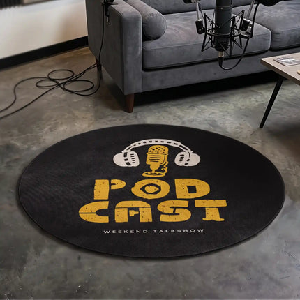 A round black rug featuring a distressed yellow and white 'PODCAST' graphic with headphones and a vintage microphone, placed on a gray concrete floor in a podcast studio setting with a gray couch and microphone visible.