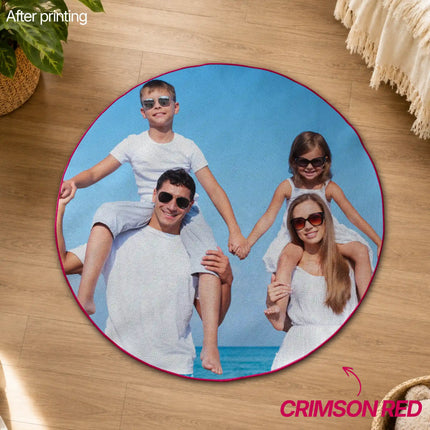 Overhead view of a round crimson red-edged custom rug printed with a family photo of a father and mother carrying two children piggyback on a beach, placed on a wood floor.