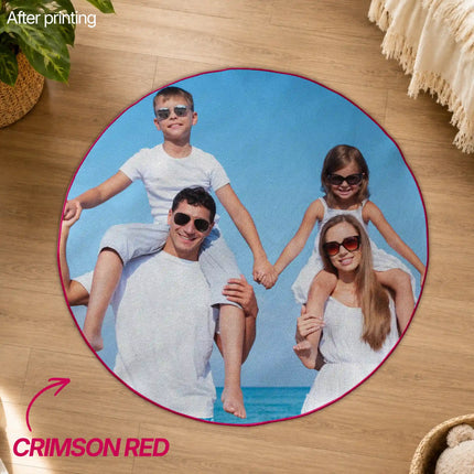 Overhead view of a round crimson red-edged custom rug printed with a family photo of a father and mother carrying two children piggyback on a beach, placed on a wood floor.