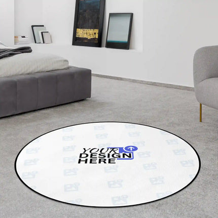 Round white rug with a 'Your Design Here' placeholder logo and jet black edge, displayed on a grey carpet in a living room.