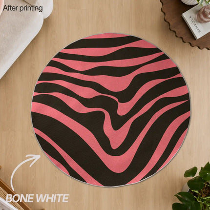 Overhead view of a round bone white-edged custom rug printed with a pink and black wavy zebra-stripe pattern, placed on a wood floor.