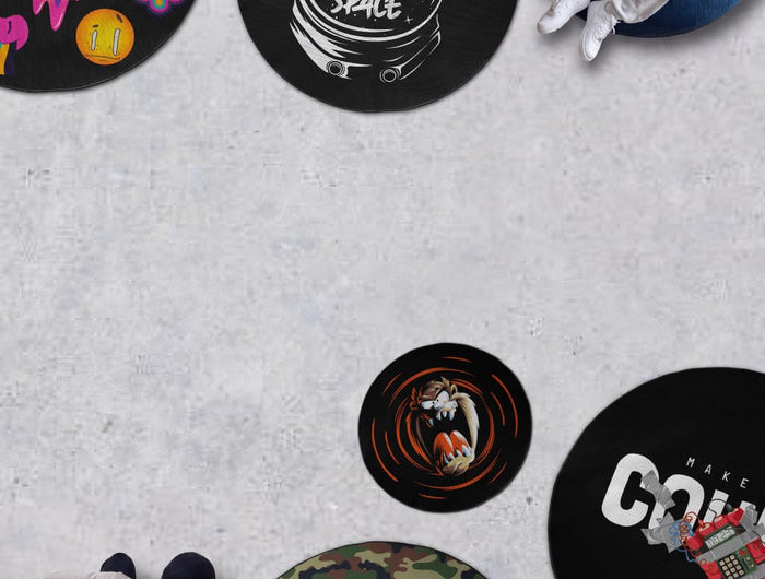 Lifestyle promotional banner featuring several round printed rugs arranged on a concrete floor. Designs include a black rug with an astronaut helmet reading "Give Me More Space," a colorful smiley-face pattern with a "30% OFF" sale badge and code "300OFF," a camouflage print, a cartoon character graphic, and a bold typography design. Two people are shown relaxing on the rugs, highlighting their size and comfort.