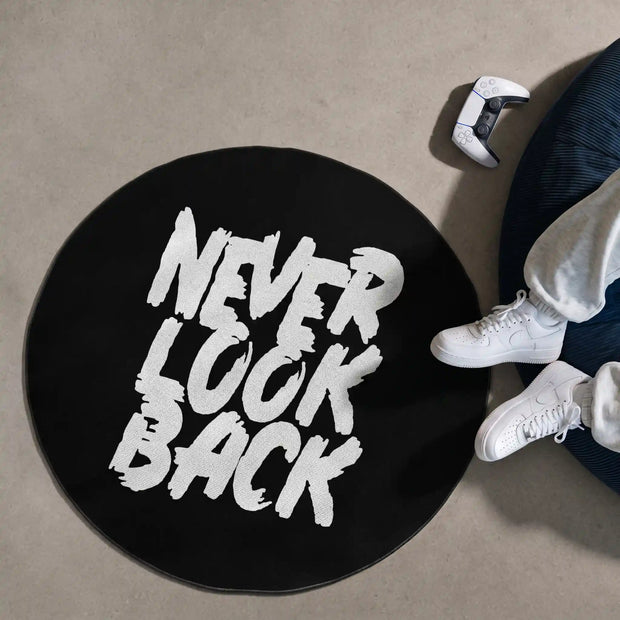 Round black gaming rug with bold white "Never Look Back" typography, displayed beside a beanbag and controller.